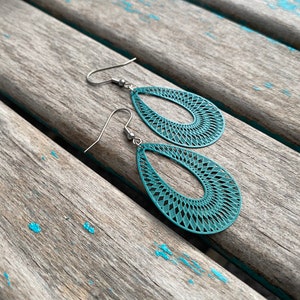 May include: Teal blue teardrop-shaped earrings with a geometric pattern. The earrings are made of metal and have a silver hook.