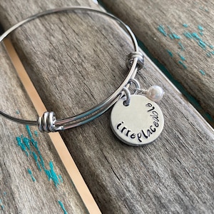 May include: A silver bangle bracelet with a charm that says "irreplaceable" and a small pearl bead.