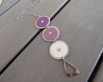 May include: A silver-toned necklace featuring three circular pendants in purple and white, each with a small, gold-colored center. The necklace has a teardrop-shaped charm at the bottom.