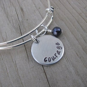 May include: Silver bangle bracelet with a charm that says "Courage" and a black bead.