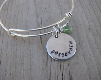 May include: Silver expandable bracelet with a round charm that says "persevere" and a small green crystal charm.