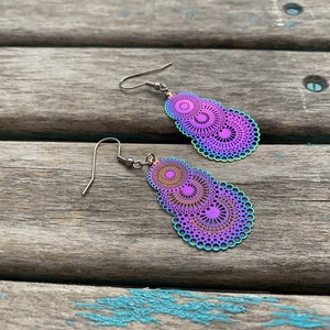 May include: A pair of iridescent earrings with a layered, circular design. The earrings are a mix of purple, blue, and gold colors.