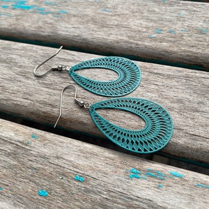May include: Teal blue teardrop shaped earrings with a delicate geometric pattern. The earrings have silver hooks.