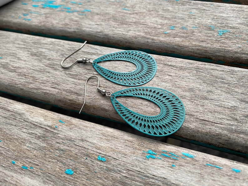 May include: Teal blue teardrop shaped earrings with a delicate geometric pattern. The earrings have silver hooks.