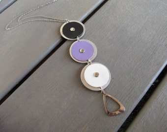 May include: A silver chain necklace with a pendant featuring three layered circular discs in black, lavender, and white. The necklace has a silver teardrop-shaped charm at the bottom.