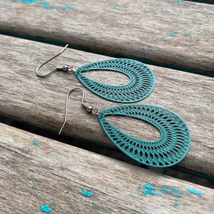 May include: Teal blue teardrop shaped earrings with a delicate geometric pattern. The earrings have silver hooks.