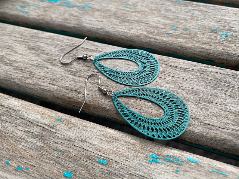 May include: Teal blue teardrop shaped earrings with a delicate geometric pattern. The earrings have silver hooks.