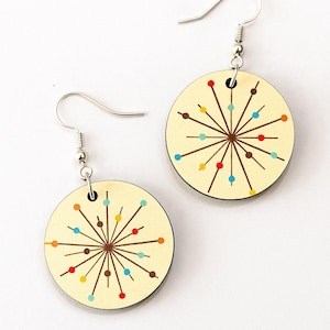 Peut inclure: Une paire de boucles d'oreilles rondes au design moderne du milieu du siècle. Chaque boucle d'oreille présente un fond crème avec un motif d'éclatement marron et des points colorés. Les boucles d'oreilles ont des crochets d'oreilles argentés.