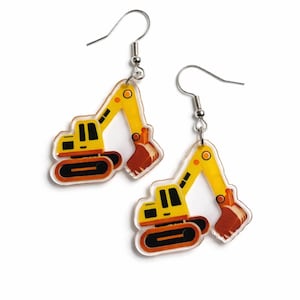 Könnte beinhalten: Ein Paar Ohrhänger mit einem gelb-orangen Bagger-Design. Die Ohrringe haben einen silbernen Haken und bestehen aus einem transparenten Material. Der Bagger hat schwarze Details und eine braune Schaufel. Ein lustiges Accessoire.