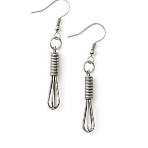 May include: A pair of silver-colored whisk earrings. Each earring features a miniature whisk design, with a coiled handle and wire loops. The earrings hang from a simple hook.