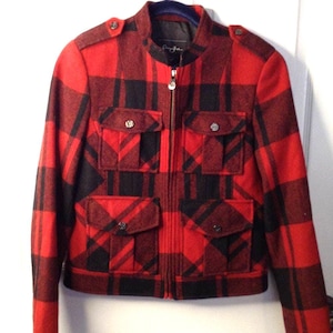 May include: Red and black plaid jacket with a zip-up front and four front pockets. The jacket has a stand-up collar and decorative buttons on the shoulders. The jacket is made of a thick, woven material.