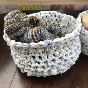 May include: Two white crocheted baskets with blue trim, one filled with brown and blue yarn, the other with cream and pink yarn.