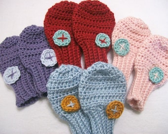 May include: Six pairs of crocheted fingerless gloves with colorful buttons. The gloves are in shades of purple, blue, pink, and red.