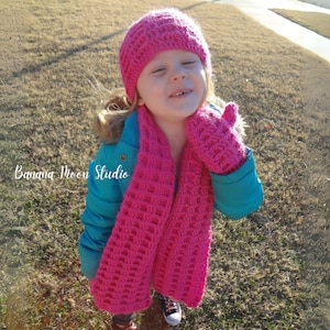 May include: A young person wearing a pink crocheted hat, scarf, and mittens. The hat and scarf have a waffle stitch pattern. The mittens are a simple crochet stitch. The person is wearing a blue jacket.