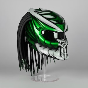 May include: A custom motorcycle helmet with a Predator design. The helmet features a glossy green and silver finish, a black visor, and black dreadlocks. It is displayed on a clear stand.