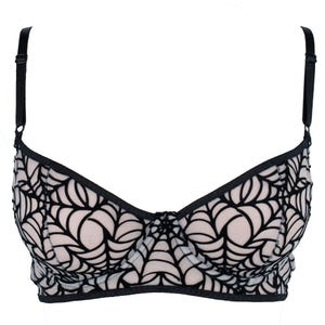 May include: A black and beige bra with a spiderweb design. The bra features adjustable black straps and a black trim. The cups are beige with a black spiderweb pattern overlay. The bra is designed with a classic silhouette.
