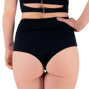 May include: Black high-waisted bottoms with a matching top. The bottoms are a solid black colour and have a high-waisted design. The top has a cut-out design with gold-coloured hardware.
