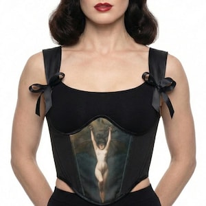 May include: A black corset top featuring wide shoulder straps adorned with small black ribbon bows. The center panel displays a printed illustration of a pale figure with wings against a dark, cloudy background. The garment has a square neckline.