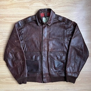 Puede incluir: Chaqueta bomber de cuero marrón con cuello, dos bolsillos delanteros y dobladillo y puños de canalé. La chaqueta tiene un diseño clásico y un aspecto vintage. El forro interior es rojo. La chaqueta es de talla mediana.