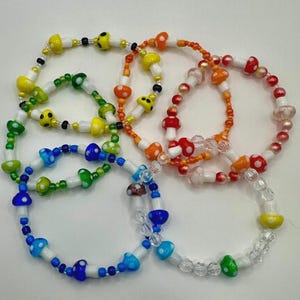 May include: A selection of colourful beaded bracelets with mushroom-shaped beads in various colours, including yellow, green, blue, orange, and red. The bracelets are strung on elastic cords and are suitable for everyday wear.