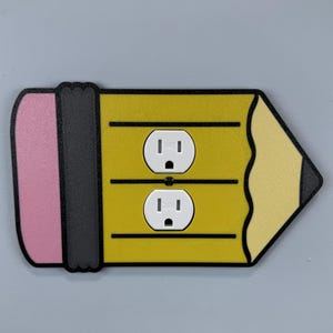 May include: A decorative pencil-shaped outlet cover. The cover features a yellow body with two white electrical outlets, a pink eraser, and a black graphite tip. The design is outlined in black.