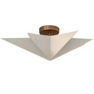 May include: A contemporary ceiling light. It features a circular brass base and a white, origami-style shade. The shade is made up of triangular panels, creating a starburst design. The light fixture is suitable for various interior styles.