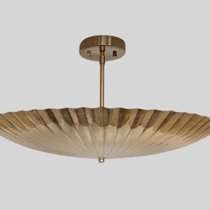以下が含まれることがあります： 真鍮色の、アールデコ様式のシーリングライト。 大きな扇形のシェードと、天井に取り付けるための中心のステムがあります。 シェードはリブ加工が施されており、下部に小さな装飾的なフィニアルが付いています。