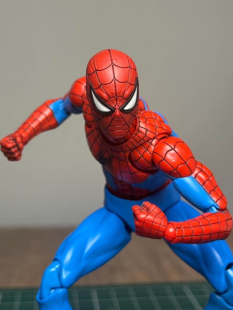 May include: A red and blue Spider-Man action figure in a dynamic pose. The figure has a red mask with white eye lenses, a red torso and arms with a web pattern, and blue pants. The figure is posed with clenched fists.
