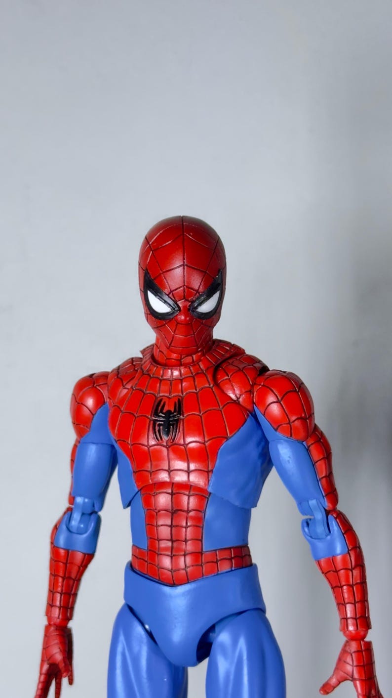 Puede incluir: Figura de acci&oacute;n detallada de Spider-Man, con un traje rojo y azul y un emblema de ara&ntilde;a negra en el pecho. La figura tiene una m&aacute;scara roja con lentes blancos. Fondo liso.
