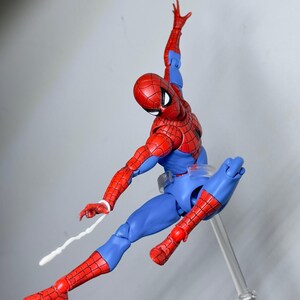 Puede incluir: Figura de acci&oacute;n de Spider-Man, rojo y azul, en pose din&aacute;mica, con un brazo levantado y una telara&ntilde;a que se extiende desde la mu&ntilde;eca. La figura presenta un patr&oacute;n texturizado y est&aacute; suspendida sobre un fondo neutro.