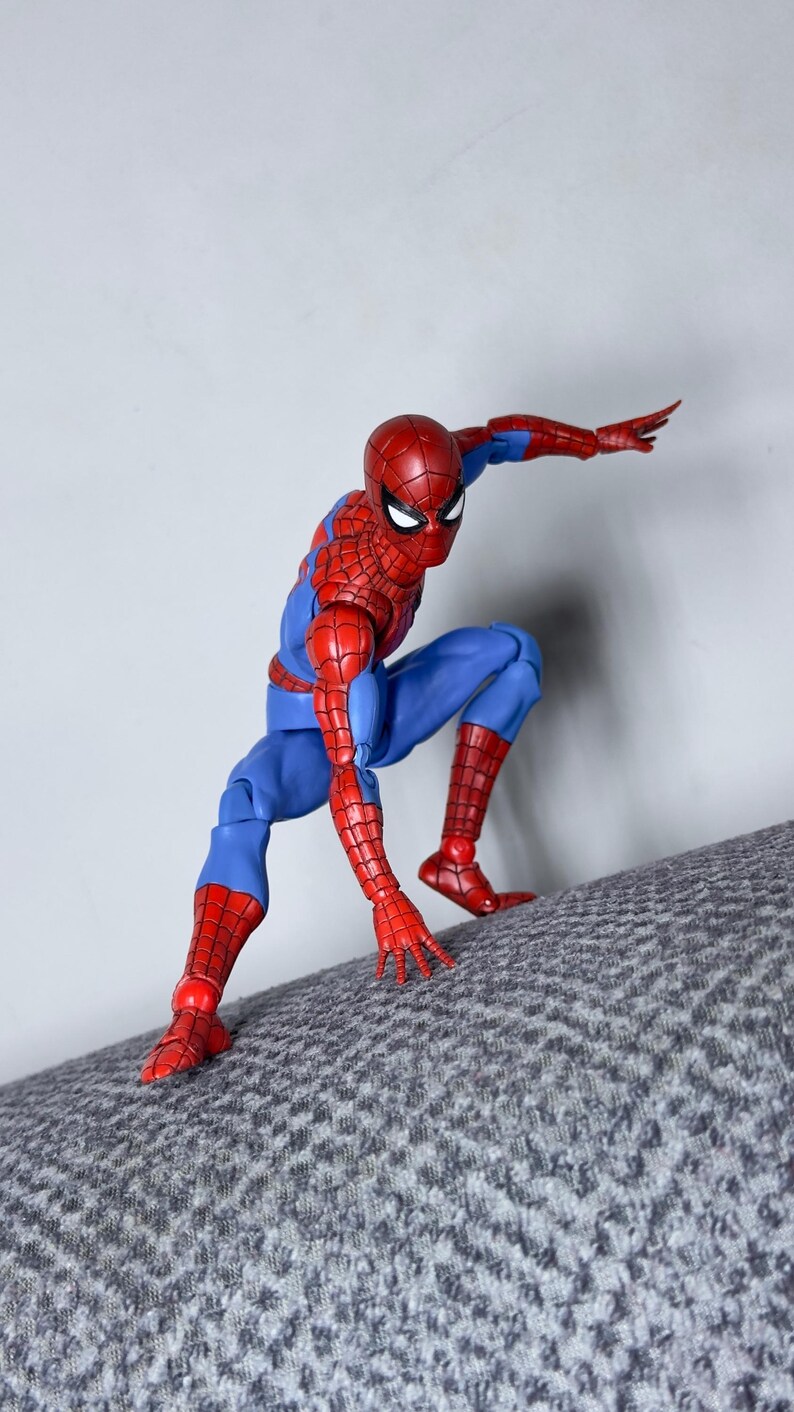 Puede incluir: Figura de acci&oacute;n de Spider-Man en una pose din&aacute;mica, vestida con un traje rojo y azul. La figura est&aacute; agachada sobre una superficie texturizada, con un brazo extendido. La m&aacute;scara de la figura tiene lentes blancos.
