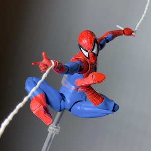 Puede incluir: Figura de acci&oacute;n de Spider-Man en una pose din&aacute;mica, suspendida en el aire. La figura es predominantemente azul y roja, con una m&aacute;scara detallada y acci&oacute;n de lanzar telara&ntilde;as. La figura est&aacute; sostenida por un soporte transparente.