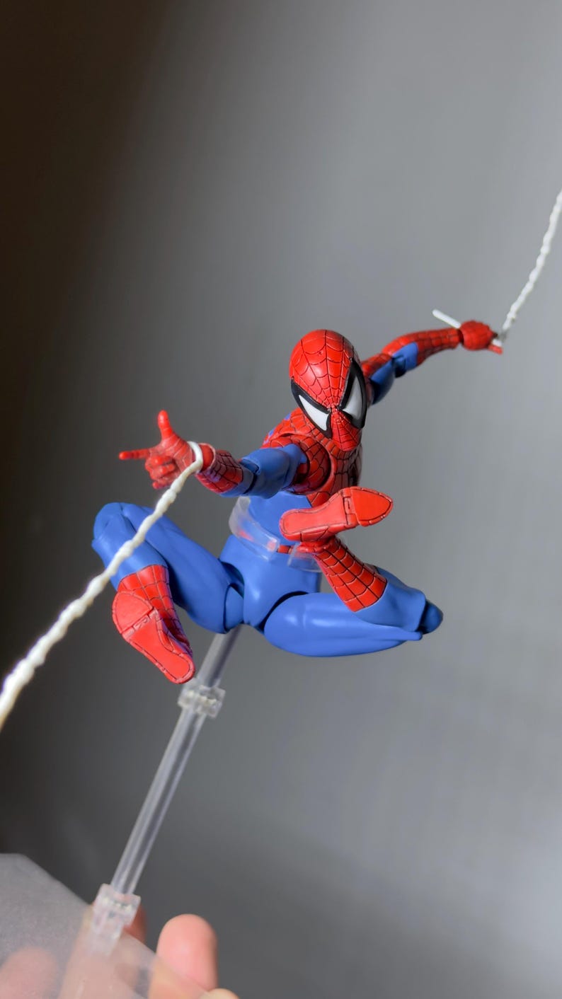 Puede incluir: Figura de acci&oacute;n de Spider-Man en una pose din&aacute;mica, suspendida en el aire. La figura es predominantemente azul y roja, con una m&aacute;scara detallada y acci&oacute;n de lanzar telara&ntilde;as. La figura est&aacute; sostenida por un soporte transparente.