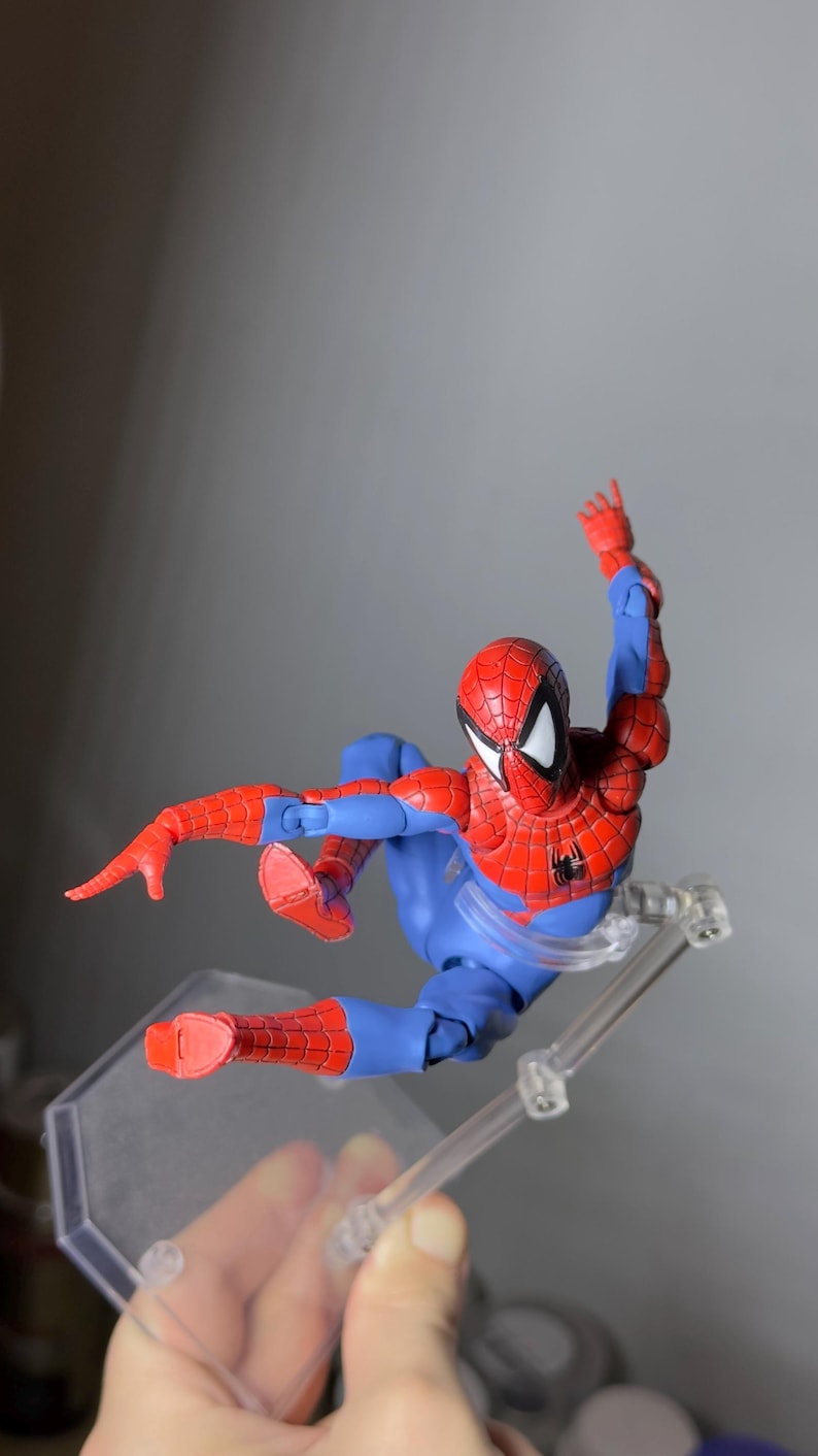 Puede incluir: Figura de acci&oacute;n de Spider-Man en rojo y azul, en una pose din&aacute;mica en el aire. La figura tiene un disfraz detallado con patrones de telara&ntilde;a y un emblema de ara&ntilde;a negra. Se apoya en un soporte de pl&aacute;stico transparente.