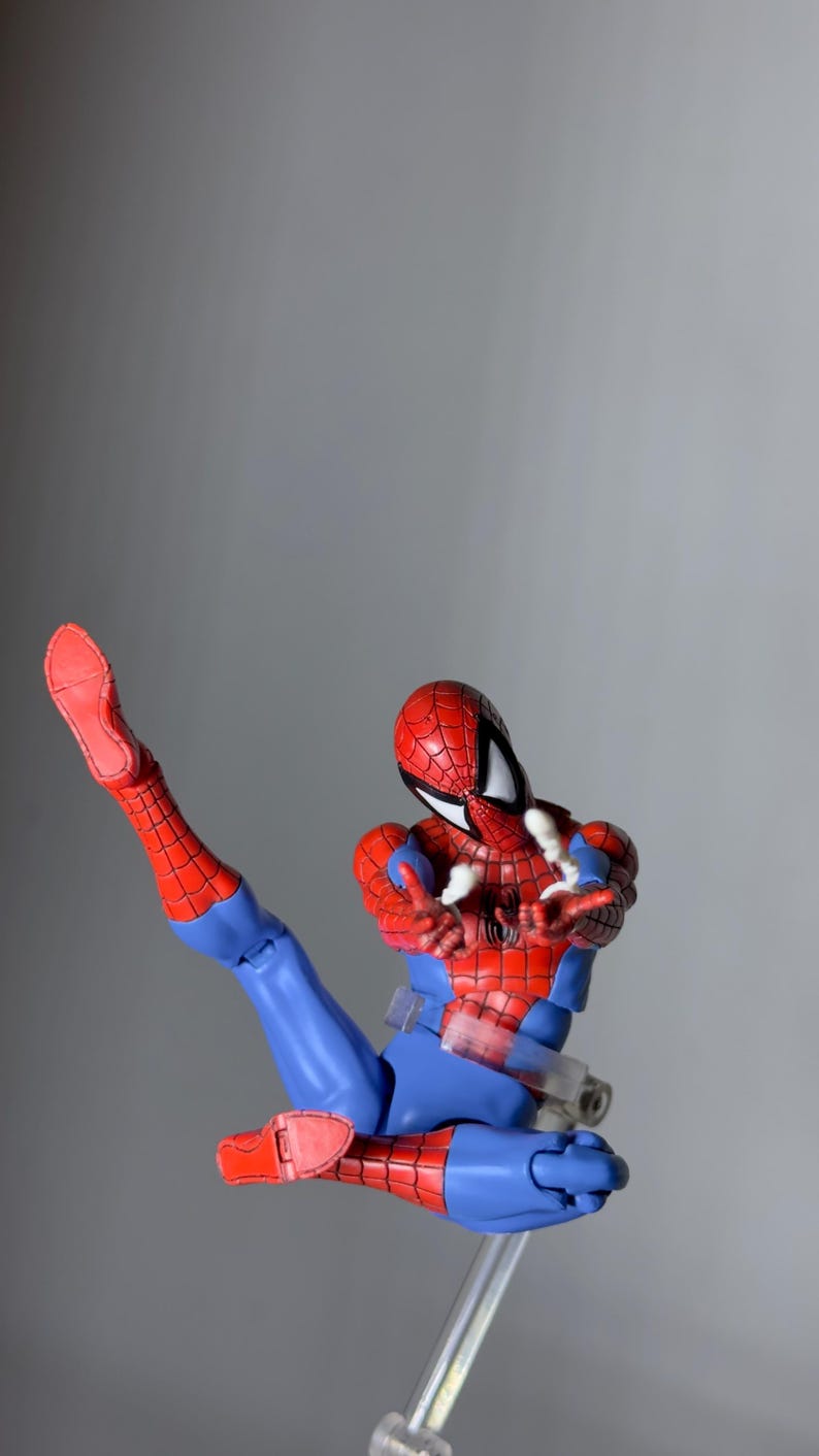 Puede incluir: Figura de acci&oacute;n de Spider-Man en una pose din&aacute;mica, con un traje rojo y azul con detalles de telara&ntilde;a. La figura est&aacute; en plena acci&oacute;n, con una pierna extendida y los brazos extendidos, sobre un fondo gris neutro.