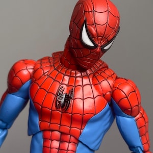 May include: A detailed action figure of Spider-Man, featuring a red and blue costume with a spider emblem on the chest. The figure has a textured, web-like pattern and white eye lenses.