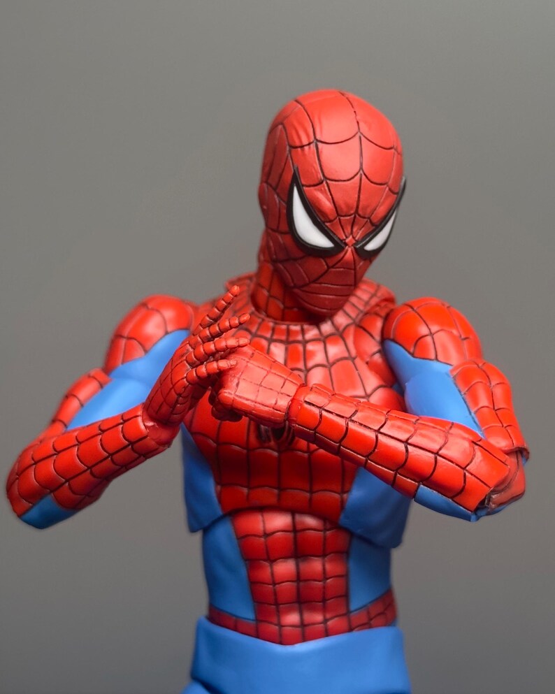 May include: A red and blue Spider-Man action figure in a dynamic pose. The figure features a detailed web pattern on the red sections of the suit, with blue accents on the arms and torso. The figure's hands are clasped together.