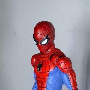 Puede incluir: Figura de acci&oacute;n de Spider-Man rojo y azul. La figura est&aacute; en una pose din&aacute;mica, con una m&aacute;scara roja y un emblema de ara&ntilde;a negra en el pecho. El disfraz de la figura presenta un patr&oacute;n de telara&ntilde;a.