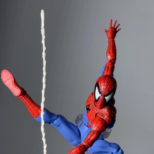 Puede incluir: Figura de acci&oacute;n de Spider-Man en una pose din&aacute;mica, vestido con un traje rojo y azul con detalles de telara&ntilde;a. La figura est&aacute; en el aire, con un brazo extendido y una hebra de telara&ntilde;a que se extiende hacia abajo. La figura mide unos 15 cm de altura.