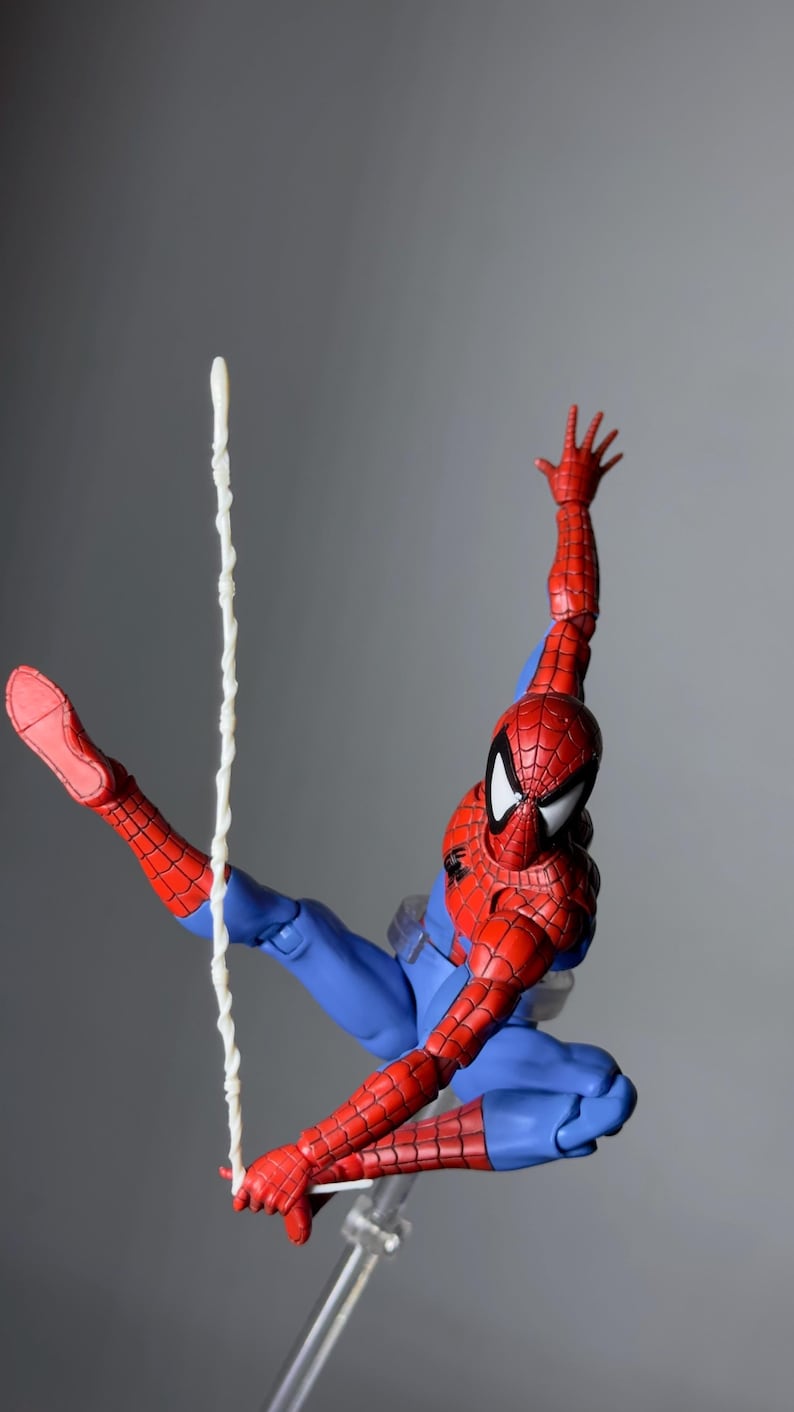 Puede incluir: Figura de acci&oacute;n de Spider-Man en una pose din&aacute;mica, vestido con un traje rojo y azul con detalles de telara&ntilde;a. La figura est&aacute; en el aire, con un brazo extendido y una hebra de telara&ntilde;a que se extiende hacia abajo. La figura mide unos 15 cm de altura.
