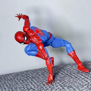 Puede incluir: Figura de acci&oacute;n de Spider-Man en pose din&aacute;mica, con traje rojo y azul. La figura est&aacute; doblada por las rodillas y la cintura, con un brazo extendido hacia arriba. Mide unos 15 cm de alto.