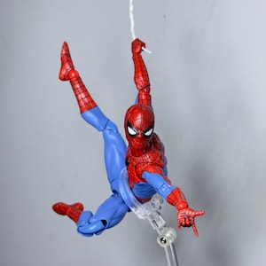 Puede incluir: Figura de acci&oacute;n de Spider-Man, rojo y azul, en pose din&aacute;mica, suspendida por una telara&ntilde;a blanca. La figura tiene m&aacute;scara, traje y botas rojas, con detalles azules. La figura mide aproximadamente 15 cm.