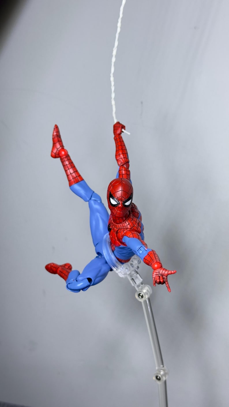 Puede incluir: Figura de acci&oacute;n de Spider-Man, rojo y azul, en pose din&aacute;mica, suspendida por una telara&ntilde;a blanca. La figura tiene m&aacute;scara, traje y botas rojas, con detalles azules. La figura mide aproximadamente 15 cm.