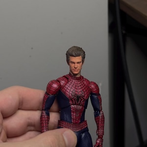 Może przedstawiać: Figurka Spider-Mana w klasycznym czerwono-niebieskim kostiumie. Figurka ma szczeg&oacute;łowy wz&oacute;r pajęczyny na czerwonych sekcjach i realistyczną rzeźbę głowy. Figurka jest trzymana w dłoni.