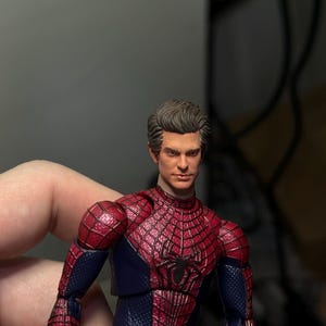 Może przedstawiać: Szczeg&oacute;łowa figurka Spider-Mana w klasycznym czerwono-niebieskim kostiumie. Figurka ma szczeg&oacute;łową twarz i dynamiczną pozę. Kostium ma na piersi emblemat pająka.