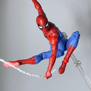 Puede incluir: Figura de acci&oacute;n de Spider-Man, rojo y azul, en pose din&aacute;mica, con un brazo extendido y una telara&ntilde;a que sale de una mano. La figura es detallada y est&aacute; sostenida por un soporte transparente.