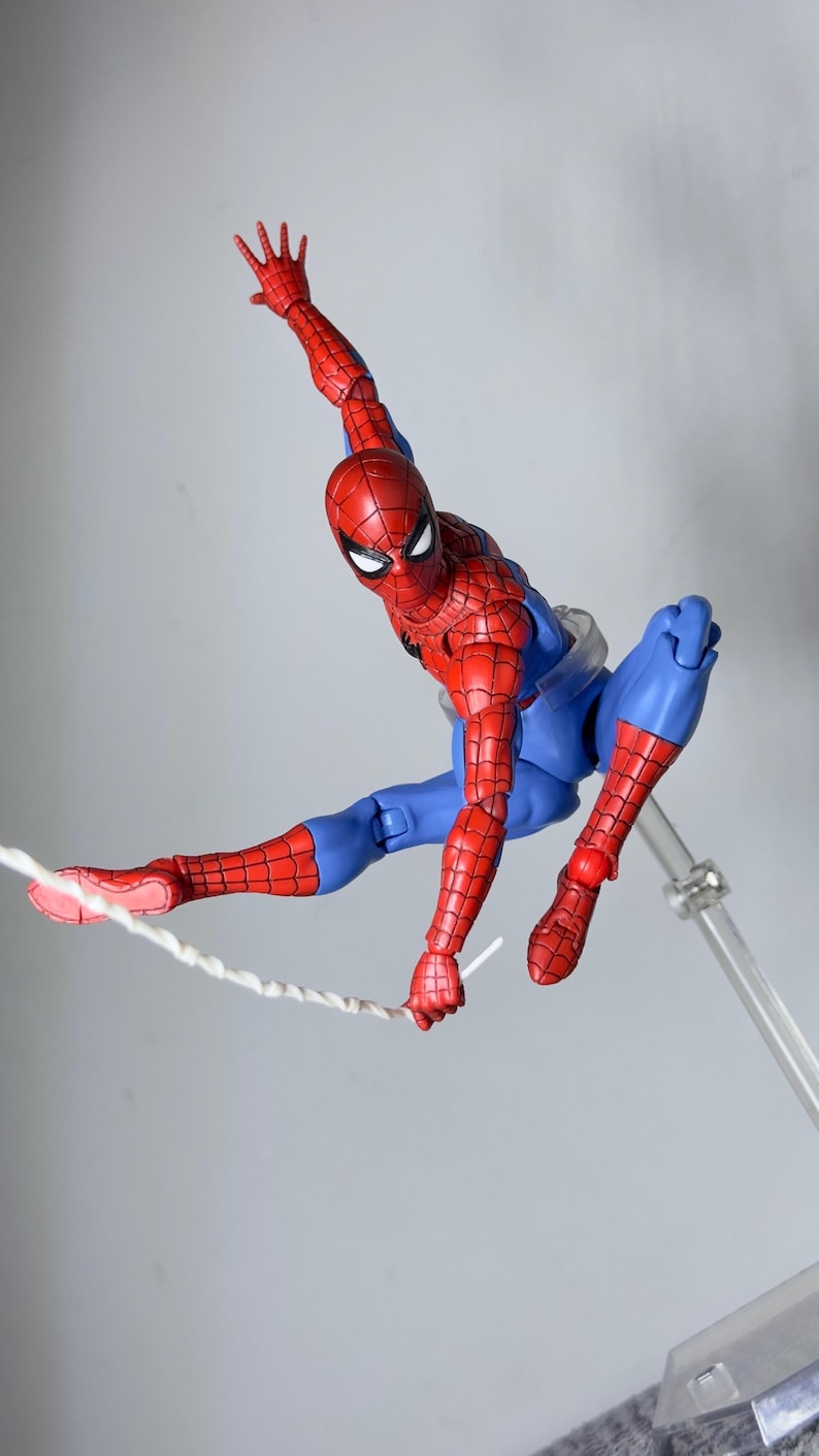 Puede incluir: Figura de acci&oacute;n de Spider-Man, rojo y azul, en pose din&aacute;mica, con un brazo extendido y una telara&ntilde;a que sale de una mano. La figura es detallada y est&aacute; sostenida por un soporte transparente.