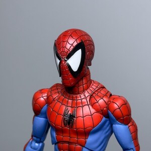 Puede incluir: Figura de acci&oacute;n detallada de Spider-Man, con un traje rojo y azul y un dise&ntilde;o de telara&ntilde;a. La figura tiene una m&aacute;scara roja con lentes blancos y un emblema de ara&ntilde;a negra en el pecho. Sobre un fondo gris.