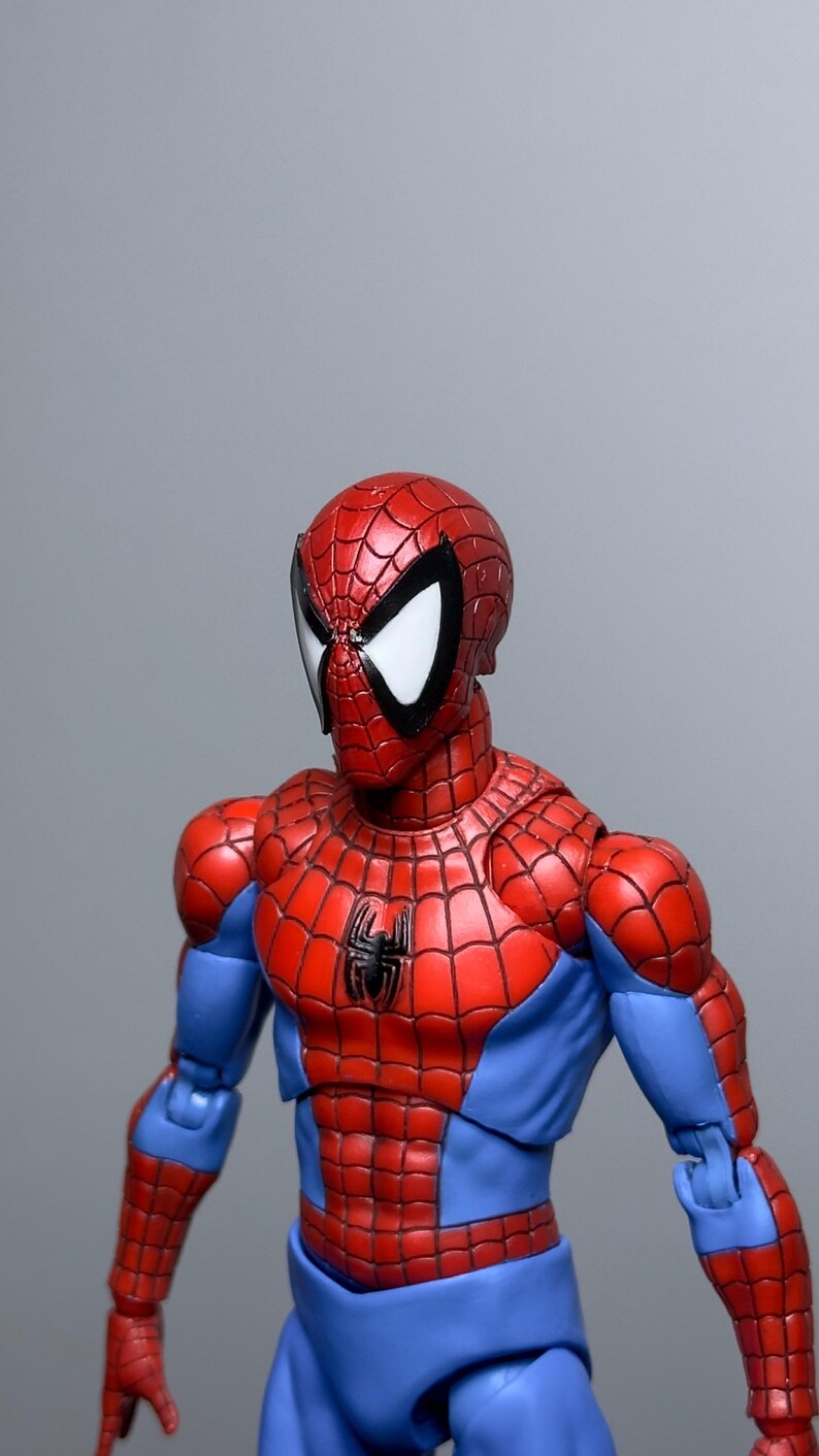 Puede incluir: Figura de acci&oacute;n detallada de Spider-Man, con un traje rojo y azul y un dise&ntilde;o de telara&ntilde;a. La figura tiene una m&aacute;scara roja con lentes blancos y un emblema de ara&ntilde;a negra en el pecho. Sobre un fondo gris.