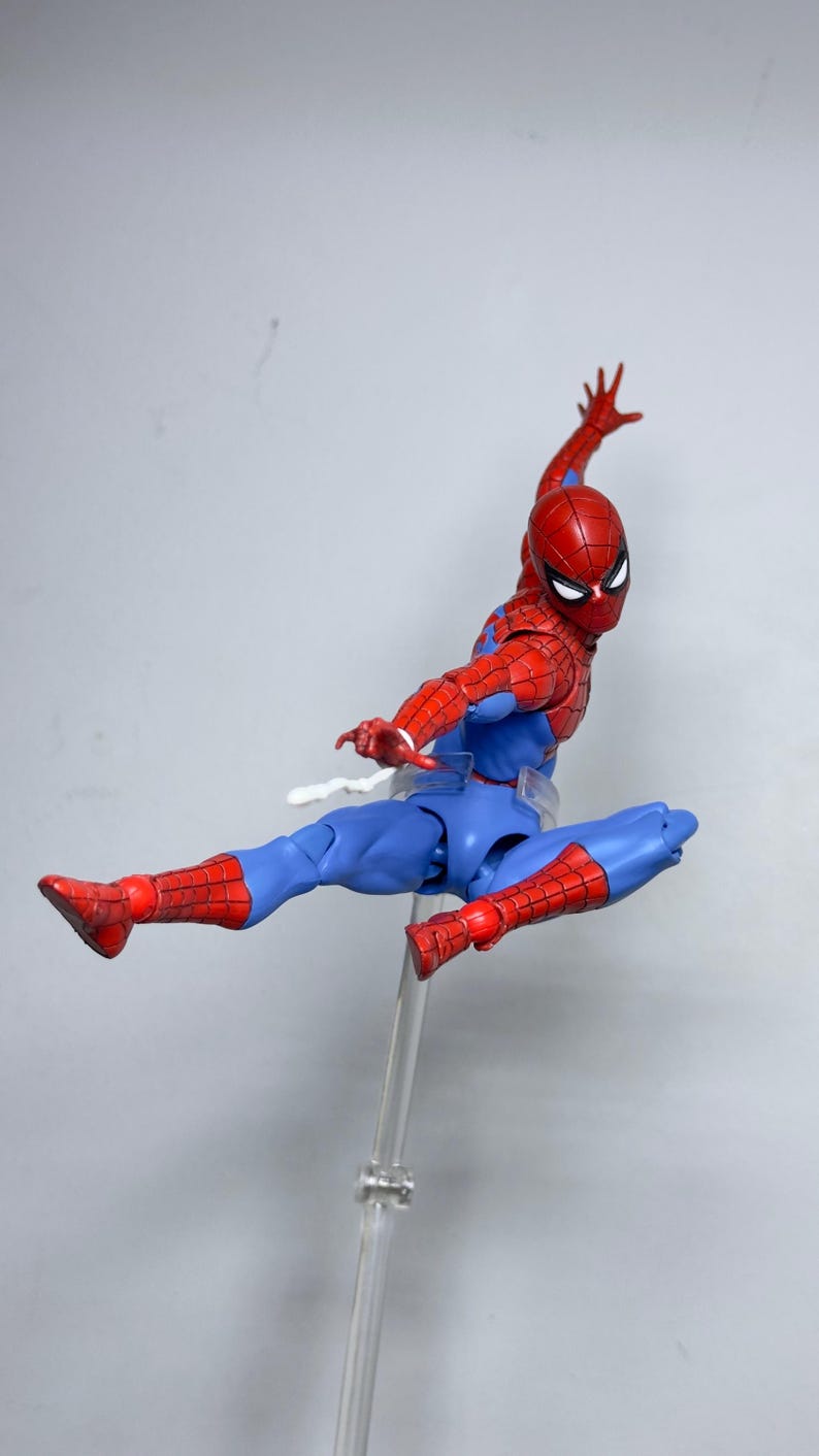 Puede incluir: Figura de acci&oacute;n de Spider-Man, rojo y azul, en una pose din&aacute;mica, suspendida en el aire. La figura presenta una m&aacute;scara, torso y extremidades rojas, con detalles azules. Montada sobre un soporte transparente, muestra el ic&oacute;nico disfraz.